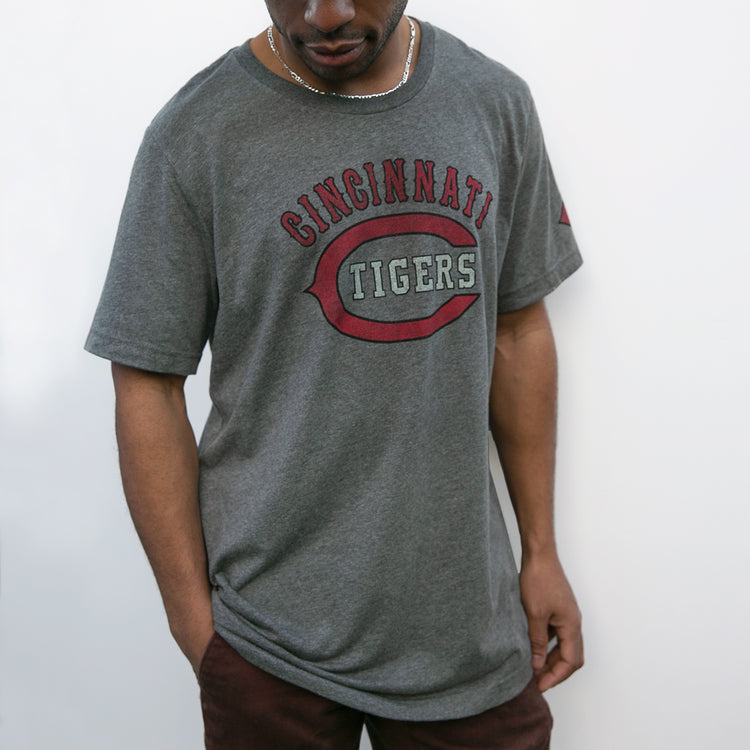 A person in an EFF Cincinnati Tigers 1934 T-Shirt, featuring red and white text on gray and a relaxed fit, stands against a white background. The historic team was once led by DeHart Hubbard; the face is partially out of frame.