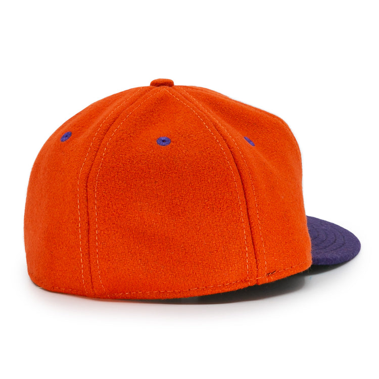 The Ebbets Field Flannels Hershey Sport Club 1956 Vintage Ballcap is orange with a dark blue brim, blue stitched eyelets, and a fabric-covered top button. Made from genuine wool baseball cloth, shown from the back for an authentic look.
