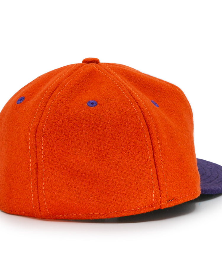 The Ebbets Field Flannels Hershey Sport Club 1956 Vintage Ballcap is orange with a dark blue brim, blue stitched eyelets, and a fabric-covered top button. Made from genuine wool baseball cloth, shown from the back for an authentic look.