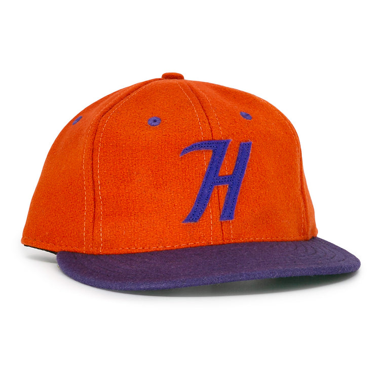The Hershey Sport Club 1956 Vintage Ballcap by Ebbets Field Flannels features an orange wool build, purple brim, and a bold purple H, inspired by the classic 1956 Hershey ballcap.