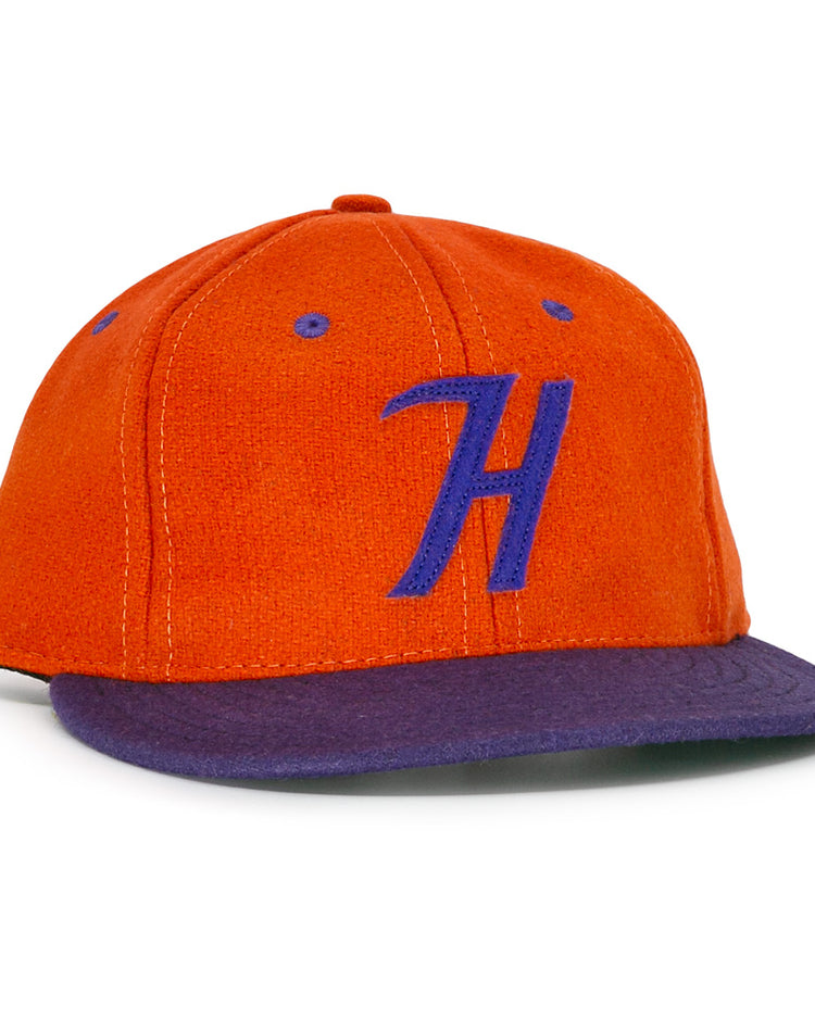 The Hershey Sport Club 1956 Vintage Ballcap by Ebbets Field Flannels features an orange wool build, purple brim, and a bold purple H, inspired by the classic 1956 Hershey ballcap.