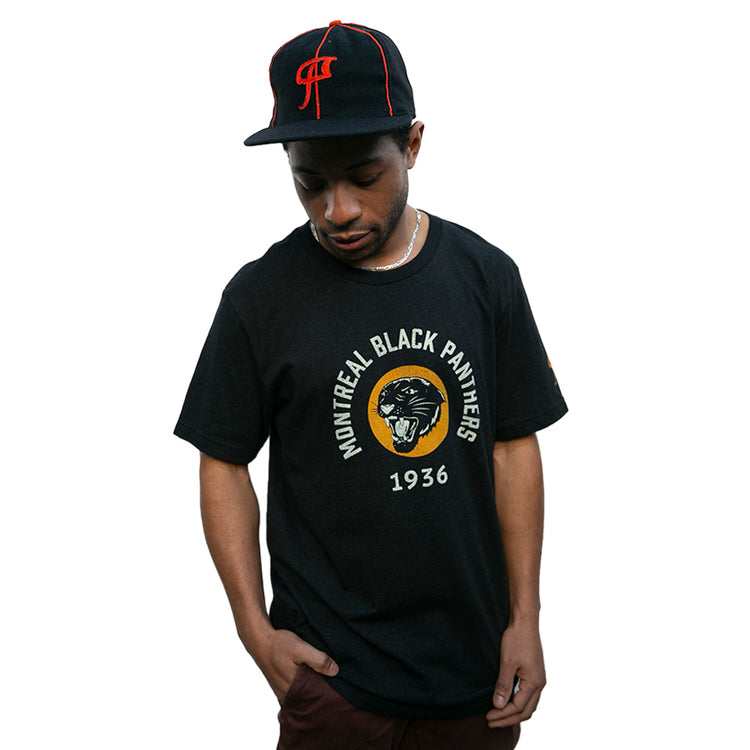 A man in an EFF Montreal Black Panthers 1936 Vintage Ballcap and a matching black T-shirt with the team name and panther logo stands against a white background, looking down.