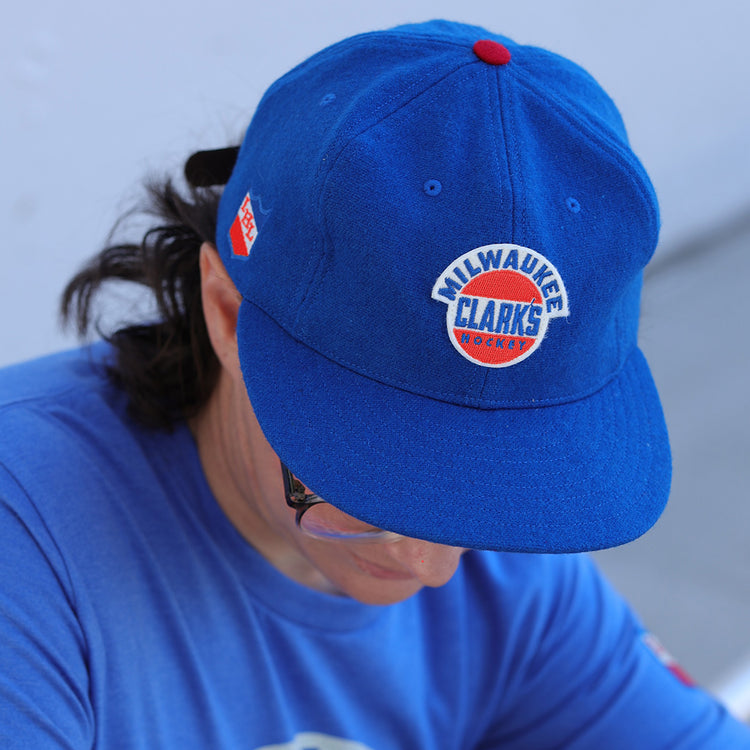 Person wearing the EFF Milwaukee Clarks Vintage Ballcap—a bright blue cap with a red and white logo patch on the front and a small red side tag—styled like a classic IHL wool cap, paired with a matching blue shirt.