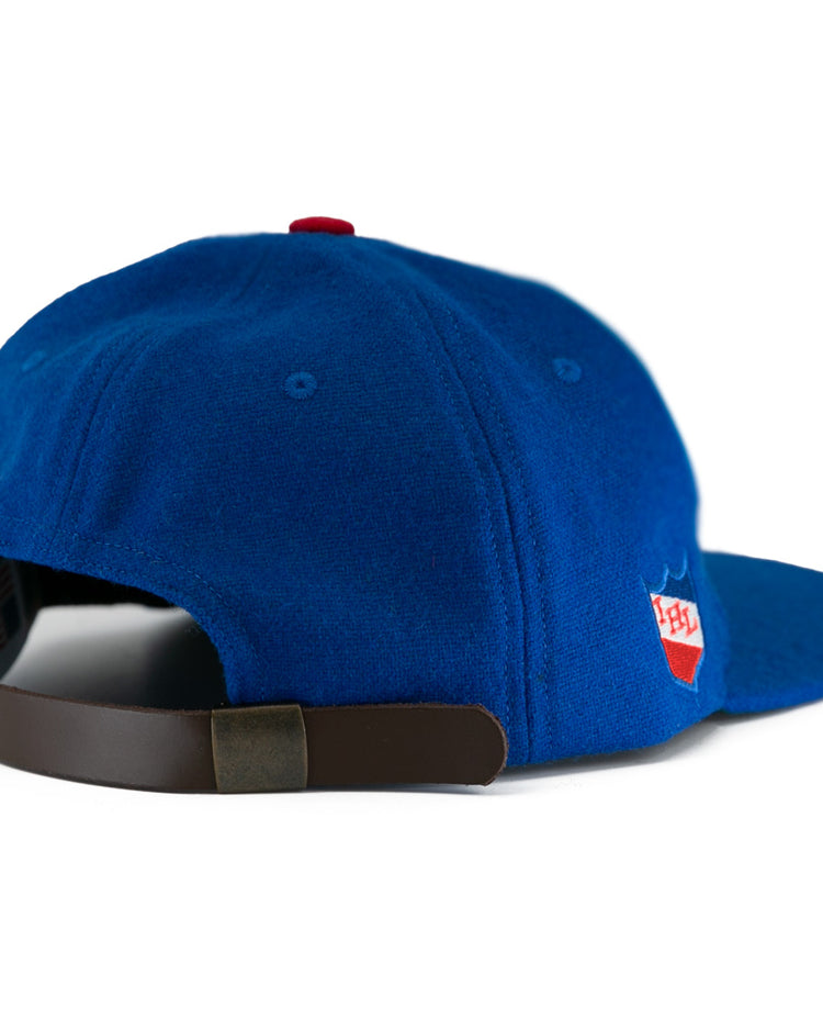 The EFF Milwaukee Clarks Vintage Ballcap is a blue wool cap with a brown adjustable strap and a red-and-white patch on the side, styled like a classic goalkeeper hat. Shown from the rear on a white background.