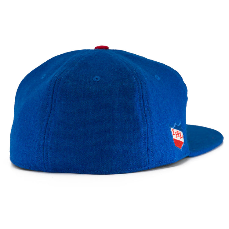 The EFF Milwaukee Clarks Vintage Ballcap is a royal blue wool hat with a red top button, viewed from the back, featuring a small red and white PH shield logo on the right side—a nod to classic goalkeeper caps.