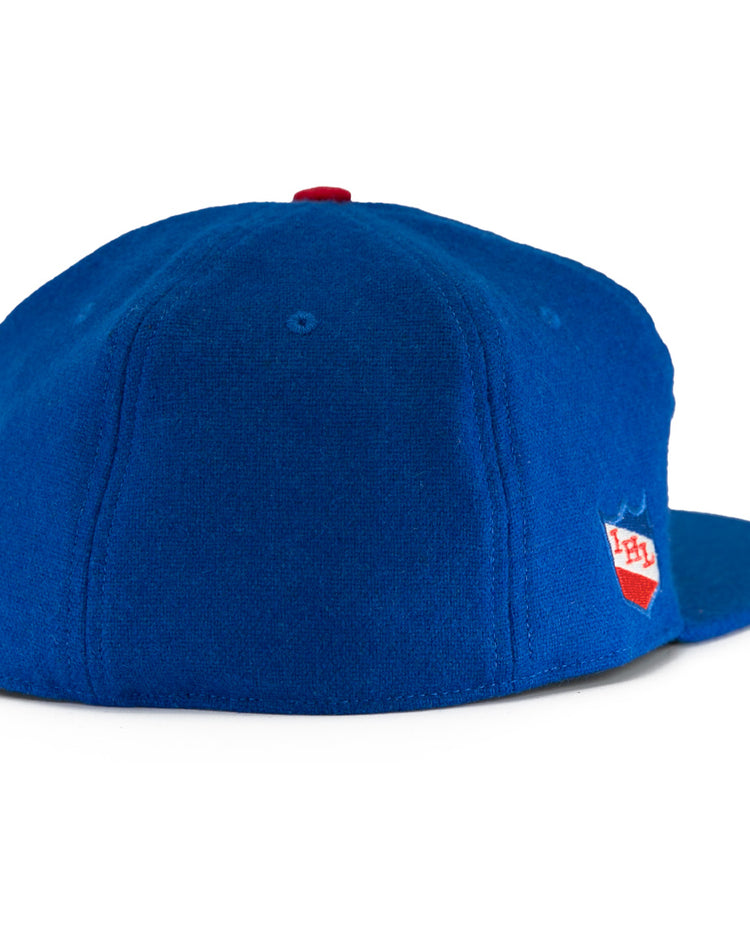 The EFF Milwaukee Clarks Vintage Ballcap is a royal blue wool hat with a red top button, viewed from the back, featuring a small red and white PH shield logo on the right side—a nod to classic goalkeeper caps.