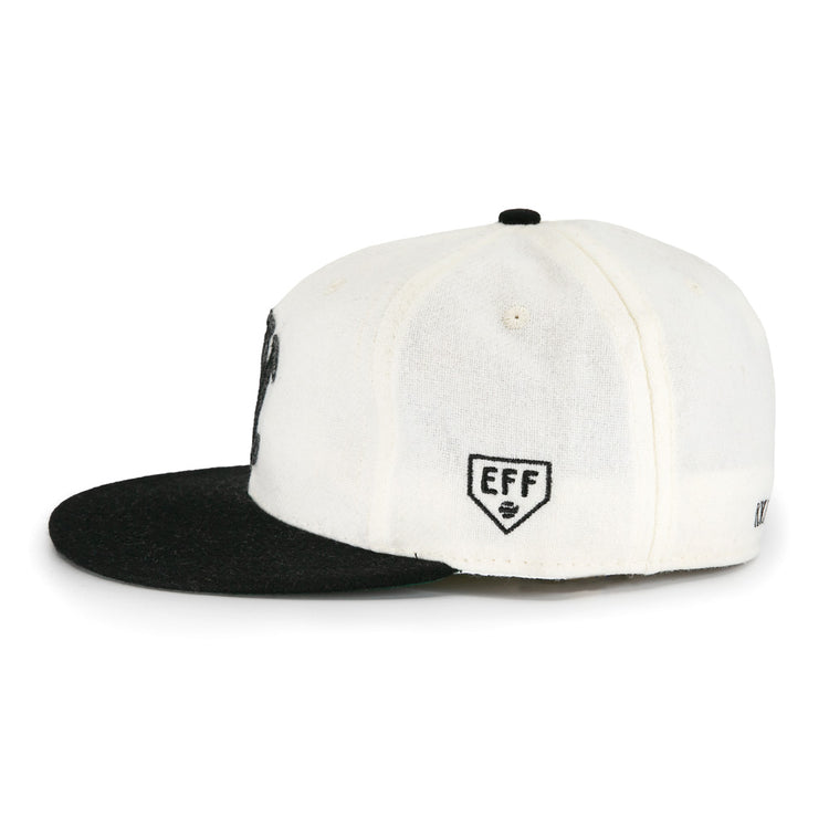 The EFF New York Knickerbockers Vintage Inspired Ballcap is shown side-on against a white background, highlighting its white crown, black flat brim, and EFF shield logo embroidered on the side panel.