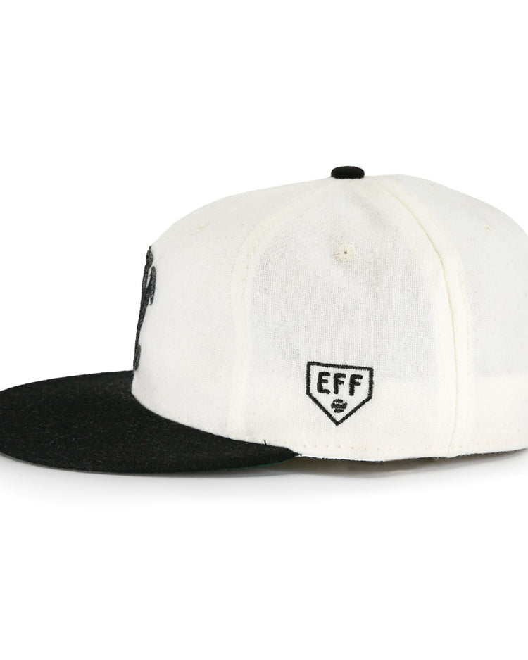 The EFF New York Knickerbockers Vintage Inspired Ballcap is shown side-on against a white background, highlighting its white crown, black flat brim, and EFF shield logo embroidered on the side panel.