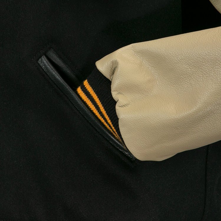 A close-up of a hand in the pocket of the EFF Pittsburgh Pirates 1960 Authentic Jacket, featuring a beige leather sleeve with a black cuff and two yellow stripes.