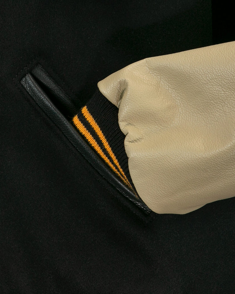 A close-up of a hand in the pocket of the EFF Pittsburgh Pirates 1960 Authentic Jacket, featuring a beige leather sleeve with a black cuff and two yellow stripes.