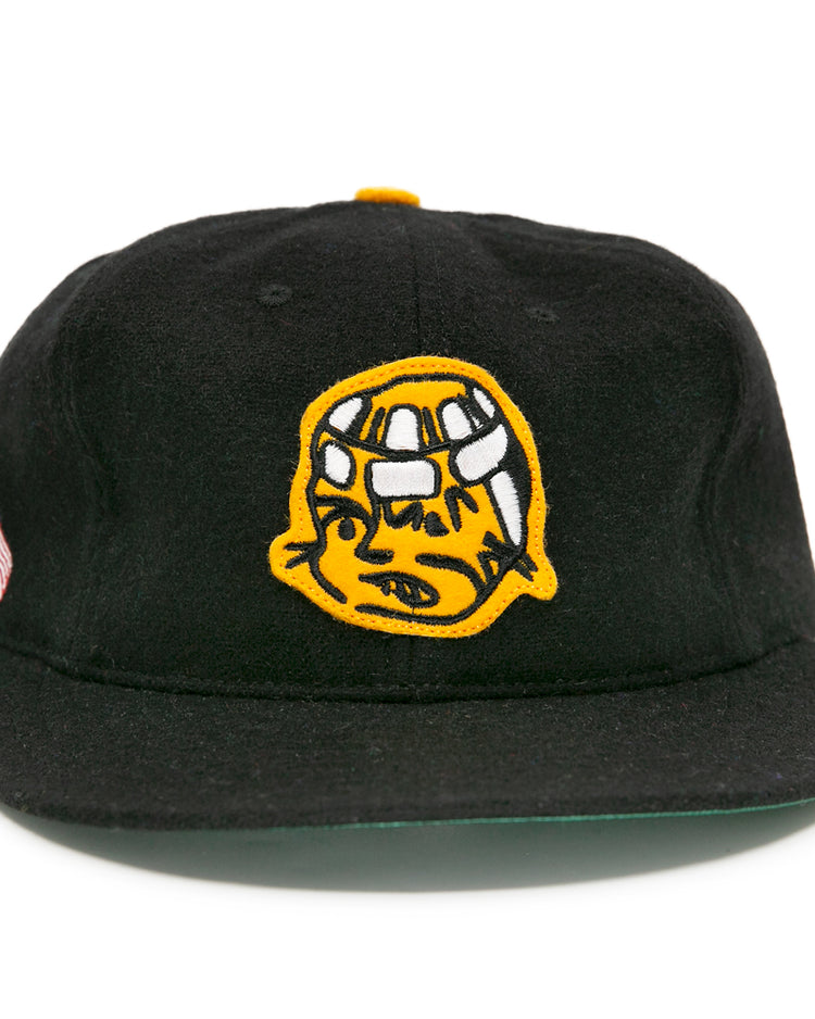 The EFF Pittsburgh Hornets 1953 Vintage Ballcap is a black wool hat featuring a yellow cartoon helmet logo on the front, plus an American flag and yellow ribbon patch on the side, inspired by classic hockey style.