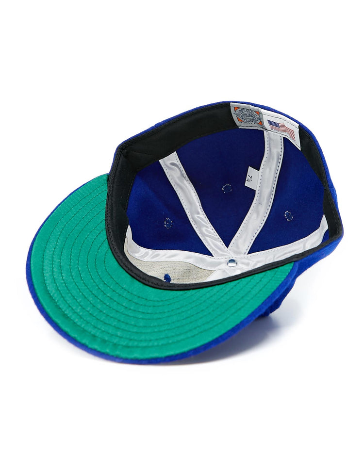 The EFF Seattle Rainiers 1941 Vintage Ballcap is shown upside down on a white background, highlighting its green underbrim, white sweatband, blue interior, and tags.