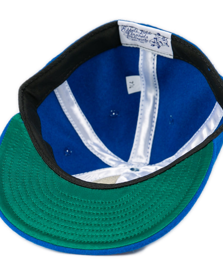 An EFF Southern Methodist University 1962 Vintage Ballcap in blue is shown upside down, displaying a green underbrim, black inner band, white satin lining, and an interior label with text and a lion graphic.