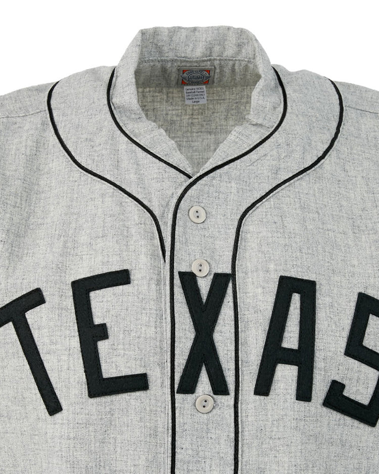 The EFF Texas Black Spiders 1938 Road Jersey is a gray vintage-style baseball jersey with black piping, large TEXAS lettering, a collar, and four white front buttons—an authentic tribute to the legendary barnstorming team.