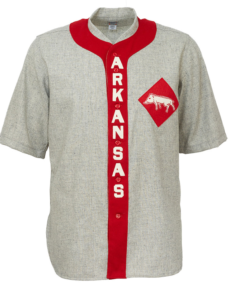 The EFF University of Arkansas 1912 Road Jersey is a gray, short-sleeve college baseball shirt with a red vertical stripe reading ARKANSAS in white and a red diamond patch featuring a white razorback logo—an authentic vintage reproduction.